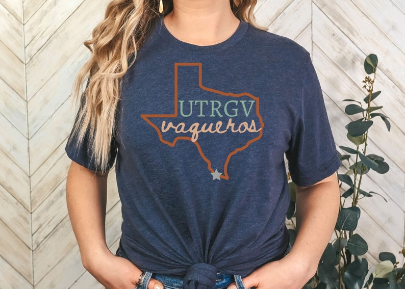 Pu&ograve; includere: T-shirt blu navy con un contorno del Texas e la scritta "UTRGV vaqueros" in arancione, verde e rosa. Una stella indica una localit&agrave; all'interno dello stato. La maglietta &egrave; girocollo e in materiale morbido.