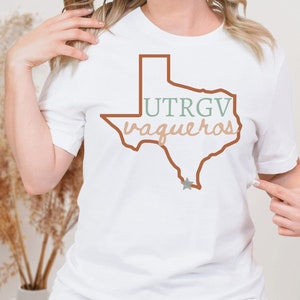 Pu&ograve; includere: T-shirt bianco con un contorno marrone dello stato del Texas e la scritta "UTRGV vaqueros" in verde e beige. Una stella grigia si trova nella parte inferiore del contorno del Texas. La maglietta &egrave; girocollo.