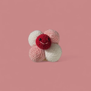 May include: A handmade, plush flower with a smiling face. The flower has a red center with a stitched smile and black eyes, surrounded by four soft, textured petals in white and pink hues. The background is a solid pink.