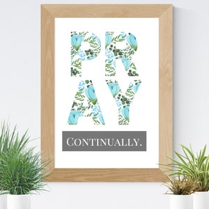 May include: A framed print with the word "PRAY" in large, blue letters with a floral pattern. The letters are on a white background and the text "CONTINUALLY." is below the letters in a smaller font.