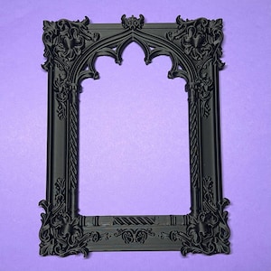 May include: A black, ornate picture frame with a gothic arch design. The frame features detailed floral and scrollwork carvings, and a twisted rope-like border. The frame is set against a purple background.