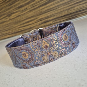May include: A decorative dog collar with a paisley pattern in shades of blue, gold, and burgundy. The collar has a soft, purple lining and a silver metal buckle. This collar is designed for pets.