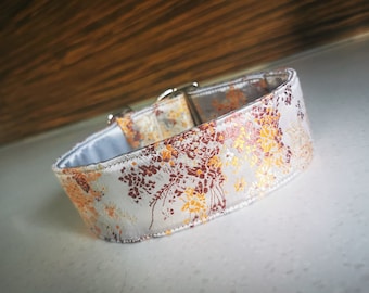 Puede incluir: Un collar de perro blanco con un patrón floral en tonos naranja y marrón. El collar está hecho de un material suave y acolchado y tiene una hebilla plateada.