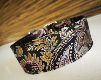 Puede incluir: Un collar para perro negro, dorado y rosa con estampado paisley y hebilla plateada.