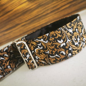 Puede incluir: Un collar de perro con estampado negro, dorado y blanco con una hebilla plateada.