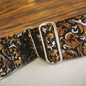 Puede incluir: Un collar de perro con estampado negro, dorado y blanco con una hebilla de metal plateado.