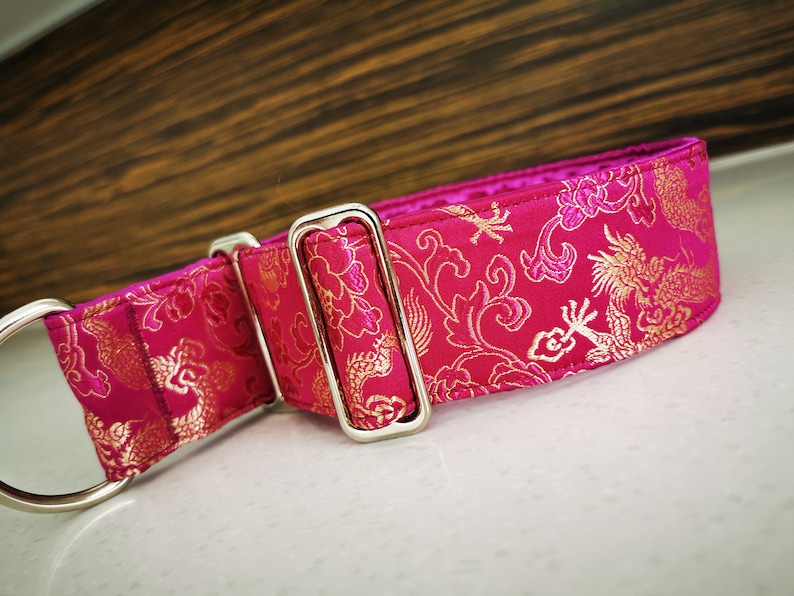 May include: A pink and gold dog collar with a dragon pattern. The collar has a silver buckle and a D-ring.