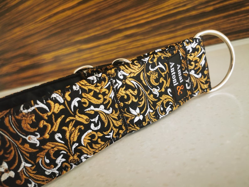Puede incluir: Collar para perro negro y dorado con estampado, herrajes plateados y el texto "Amal & Antoni" en la correa.