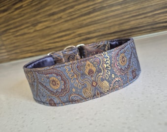May include: A decorative dog collar with a blue, gold, and burgundy paisley pattern. The collar has a soft, blue interior and silver metal hardware. The collar is designed for a medium to large dog.