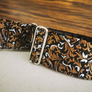 Puede incluir: Un collar de perro con estampado negro y dorado con una hebilla plateada.