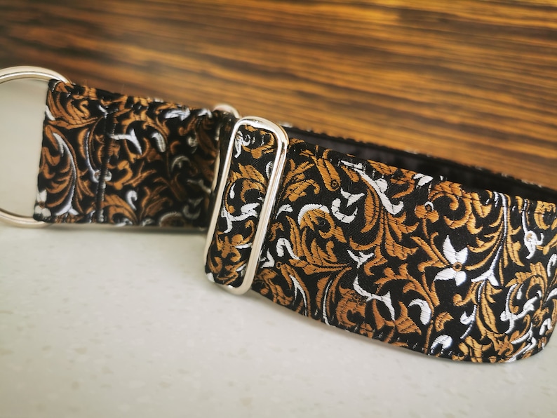 Puede incluir: Un collar de perro con estampado negro y dorado con una hebilla plateada.