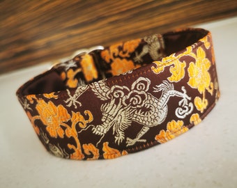 Puede incluir: Un collar para perro marrón y dorado con un diseño de dragón blanco. El collar está hecho de una tela suave y duradera y tiene un cierre de hebilla seguro.