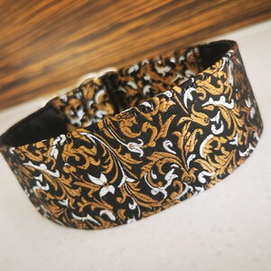 Puede incluir: Un collar para perro negro, dorado y blanco con un dise&ntilde;o floral.