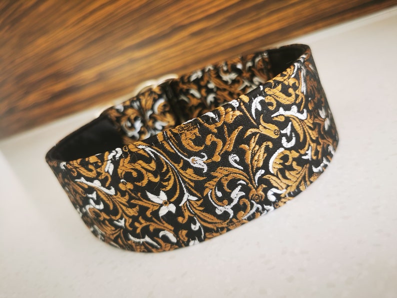 Puede incluir: Un collar para perro negro, dorado y blanco con un dise&ntilde;o floral.