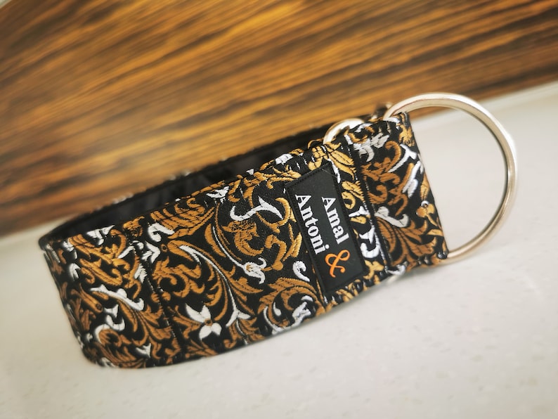 Puede incluir: Collar para perro de patr&oacute;n negro y dorado con un anillo en D plateado y el texto "Amal & Antoni" en una etiqueta negra.