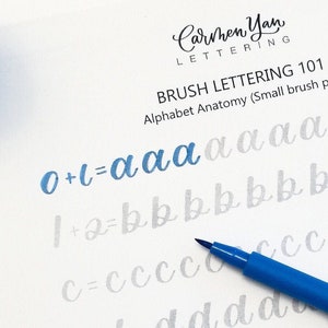 Può includere: Un primo piano di una guida di calligrafia con pennello con una penna a pennello blu. La guida mostra l'alfabeto in corsivo con le lettere 'a', 'b', 'c', 'd', 'e', 'f', 'g' e 'h' scritte più volte. Il testo sulla pagina dice 'Brush Lettering 101 Alphabet Anatomy (Small brush pen)'