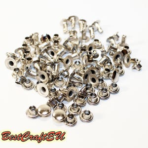 May include: A large pile of silver metal rivets, some with a domed top, and some with a flat top. The rivets are scattered on a white surface.