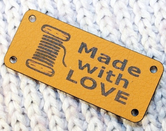 Può includere: Un'etichetta in pelle marrone con un rocchetto di filo nero e il testo "Made with LOVE".