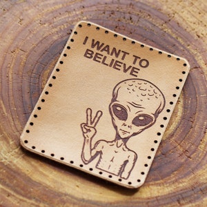 May include: A brown leather patch with the text "I WANT TO BELIEVE" and a cartoon alien with a peace sign.