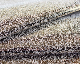 May include: Close-up of a gold fabric with a white, textured, cracked pattern. The fabric is folded in half, showing the pattern on both sides.