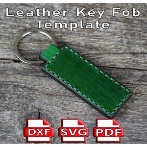May include: A green leather key fob template with a silver key ring. The key fob is rectangular with a stitched border. The text "Leather Key Fob Template" is at the top. Below are icons for DXF, SVG, and PDF file formats.