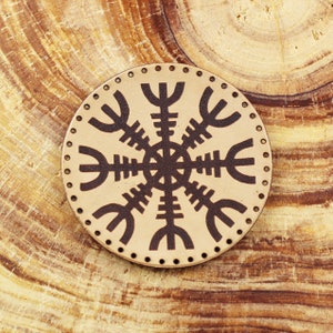May include: A round, beige leather patch with a brown Vegvisir symbol, a Norse directional symbol, in the centre. The patch is surrounded by a row of small, evenly spaced dots.