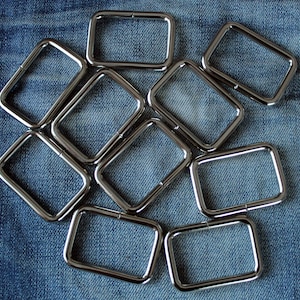 May include: Ten silver metal D-rings arranged in a circular pattern on a blue denim background.
