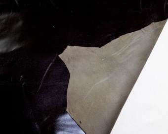 May include: A close-up of a piece of black leather with a lighter brown section folded over. The leather has a smooth, textured surface.