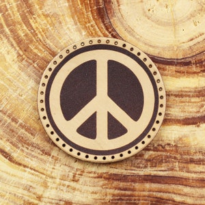 May include: A brown leather patch with a white peace sign in the centre. The patch has a circle of small white dots around the edge.