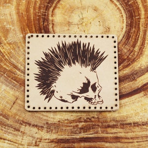 May include: A brown leather patch with a black and white image of a skull with a mohawk. The patch has a stitched border.
