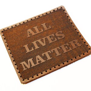 May include: Brown leather patch with the text "ALL LIVES MATTER" embossed in white.