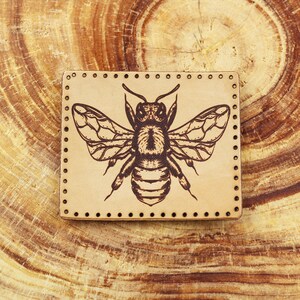 May include: A brown leather patch with a detailed illustration of a bee in black and brown. The patch has a stitched border.