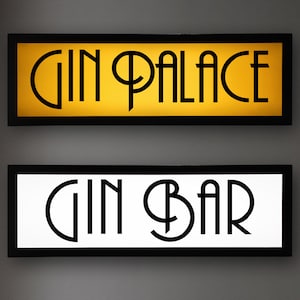 May include: Two rectangular wall signs with black frames. The top sign features a gold background with the black text GIN PALACE in a stylized font. The bottom sign features a white background with the black text GIN BAR in the same font style.