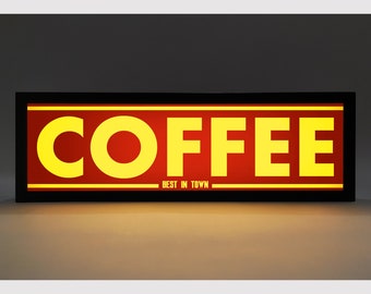 May include: A black framed sign with a red background and yellow text that reads "COFFEE BEST IN TOWN".