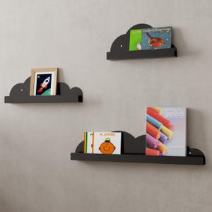 Peut inclure: Trois étagères en forme de nuage noires montées sur un mur gris. L'étagère du haut contient un livre intitulé "Georges le Rouge-Gorge". L'étagère du milieu contient un cadre photo représentant une fusée. L'étagère du bas contient deux livres, l'un intitulé "M. JOYEUX" et l'autre intitulé "Dessiner avec des pastels".