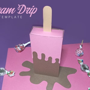 Puede incluir: Una plantilla de caja con forma de cono de helado rosa y marrón para un favor de fiesta o un regalo. La caja está diseñada para parecerse a un cono de helado derretido con un goteo de chocolate marrón. La caja está sobre una superficie rosa con caramelos esparcidos a su alrededor.