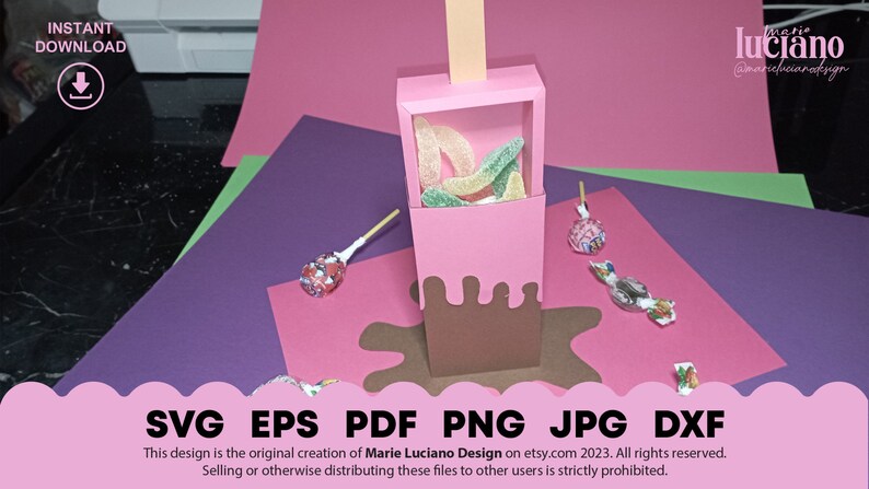 May include: A pink and brown paper craft box shaped like an ice cream cone with a brown chocolate drip. The box is filled with green and yellow gummy candies. The box is sitting on a pink surface with a brown chocolate drip around it.