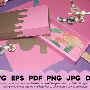 May include: A pink and brown popsicle-shaped box with a lid. The box is open and filled with gummy candies. The box is sitting on a purple surface.