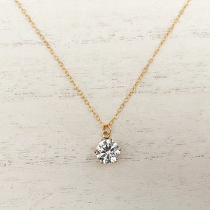 May include: A gold chain necklace with a single large clear cubic zirconia pendant.