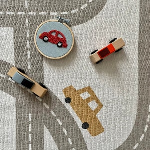 May include: A gray and white play mat with a gray road design. There are three toy cars on the mat, one red, one brown, and one gray.