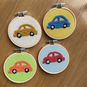 May include: Four embroidery hoops with different colored cars inside. The cars are made with yarn and are different colors: yellow, blue, red, and orange.