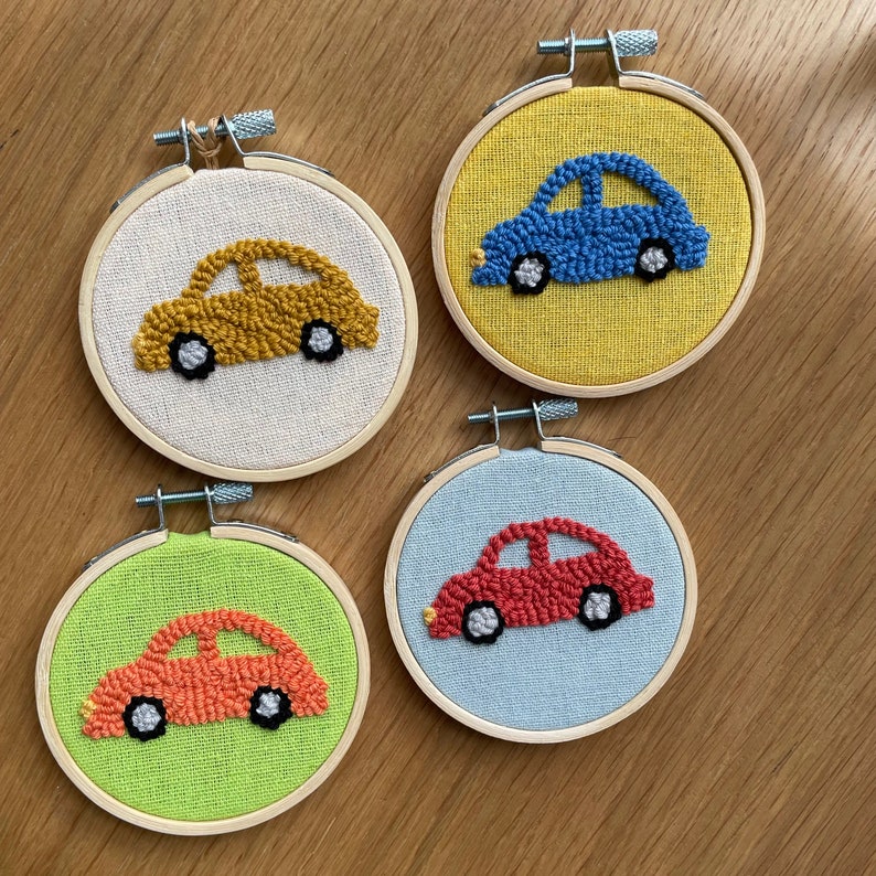 May include: Four embroidery hoops with different colored cars inside. The cars are made with yarn and are different colors: yellow, blue, red, and orange.