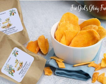 May include: A white bowl filled with bright orange dried mango slices sits on a blue cloth. Scattered around are more mango pieces. Two brown paper bags with "Mango Passion" labels are also visible, suggesting a food product.