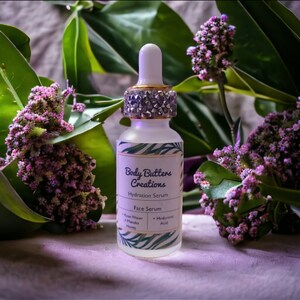 Może przedstawiać: Przezroczysta butelka szklana z pozłacanym i srebrnym korkiem, z etykietą "Body Butters Creations Serum nawilżające Serum do twarzy Woda r&oacute;żana + Mi&oacute;d marula + Kwas hialuronowy".