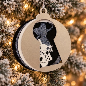 Könnte beinhalten: Ein mehrschichtiger, runder Weihnachtsbaumschmuck mit einer schlüssellochförmigen Ausstanzung. Das Design zeigt eine glitzernde blaue Silhouette einer Figur und eine weiße Schicht mit einem Kaninchen, das eine Trompete hält.