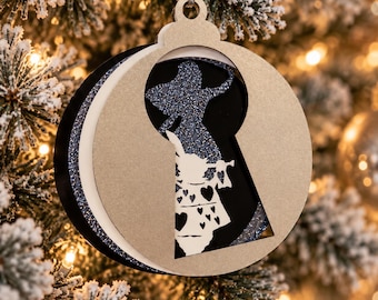 Puede incluir: Un adorno navideño circular de varias capas con un recorte en forma de cerradura. El diseño incluye una silueta azul brillante de un personaje y una capa blanca que representa a un conejo sosteniendo una trompeta con corazones.