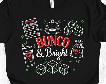 Op de afbeelding: Zwart T-shirt met een kleurrijk grafisch ontwerp met de tekst "Bunco & Bright". Het ontwerp bevat dobbelstenen, een bel, een scorekaart en een geldbuidel, allemaal in een speelse stijl. Het shirt is gemaakt van zacht materiaal.