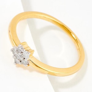 Puede incluir: Un anillo de banda de oro con un pequeño racimo de diamantes engastados en forma de flor.