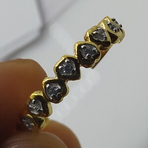 May include: A gold band ring with a row of small, clear heart-shaped stones.