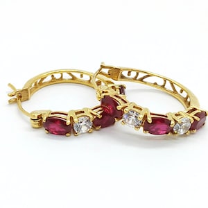 May include: Gold hoop earrings with red and white cubic zirconia stones.